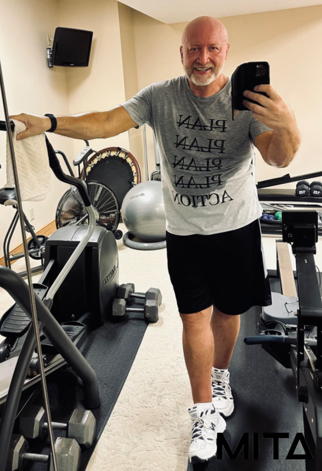 Man taking a selfie in a home gym, wearing workout clothes and smiling.