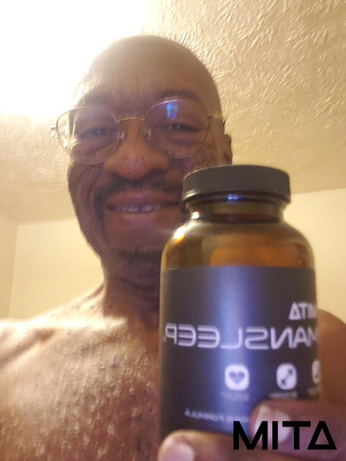 A person smiling and holding a bottle of MITA supplements.